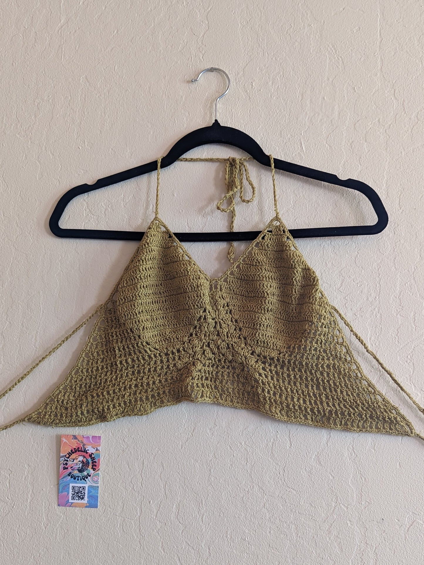 Green crochet top hung on a white wall.