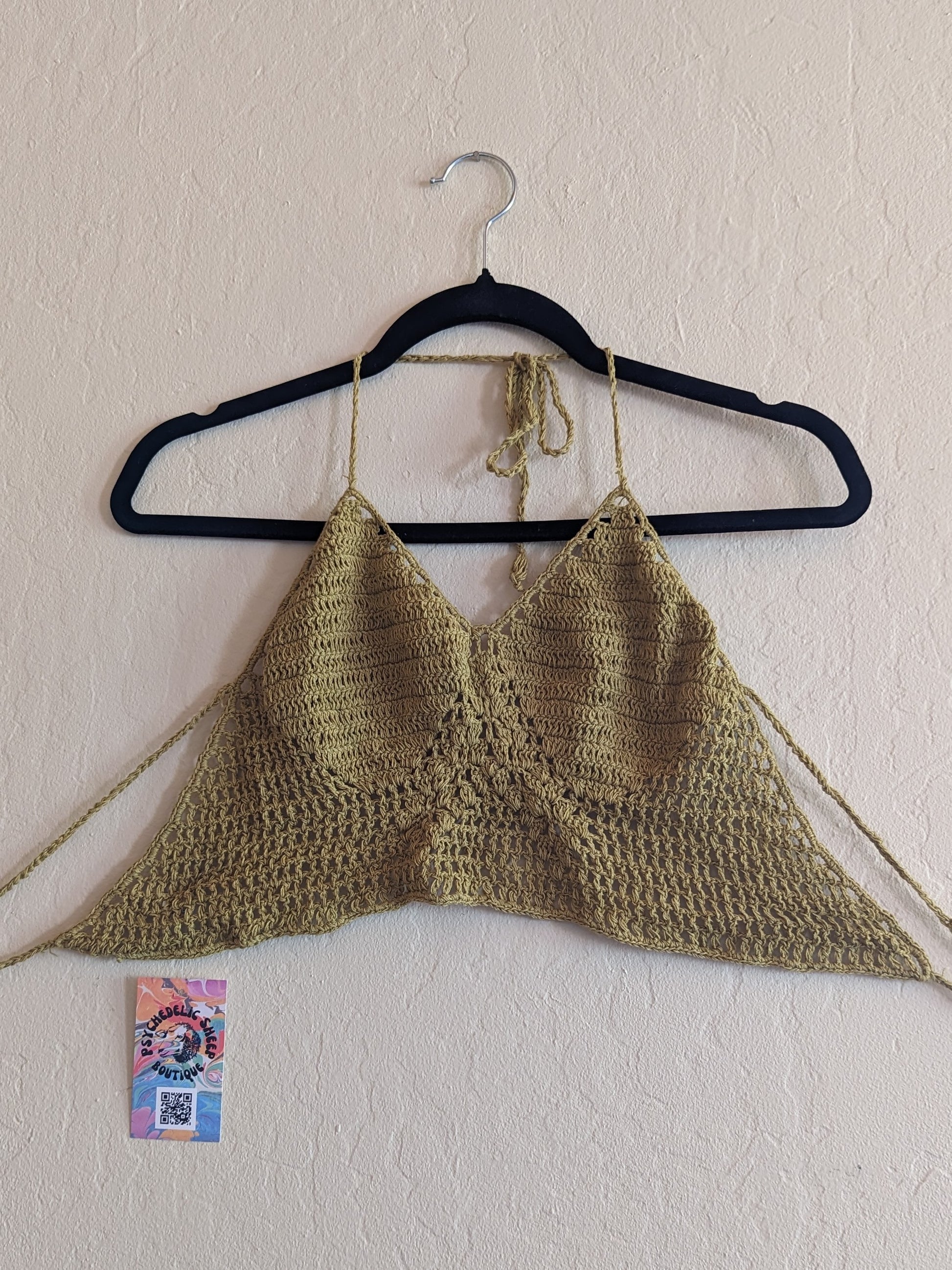 Green crochet top hung on a white wall.