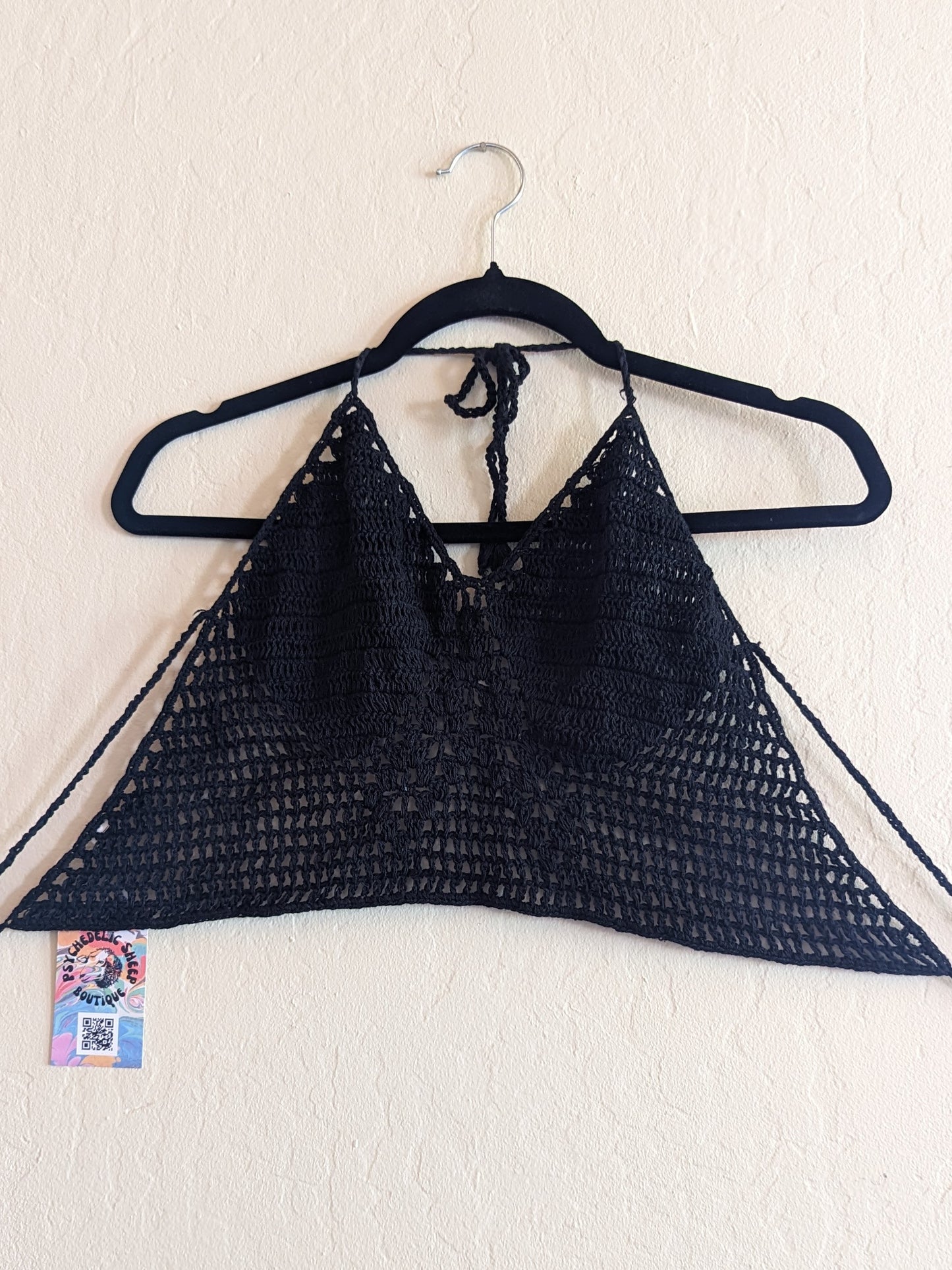 Black crochet top hung on a white wall.