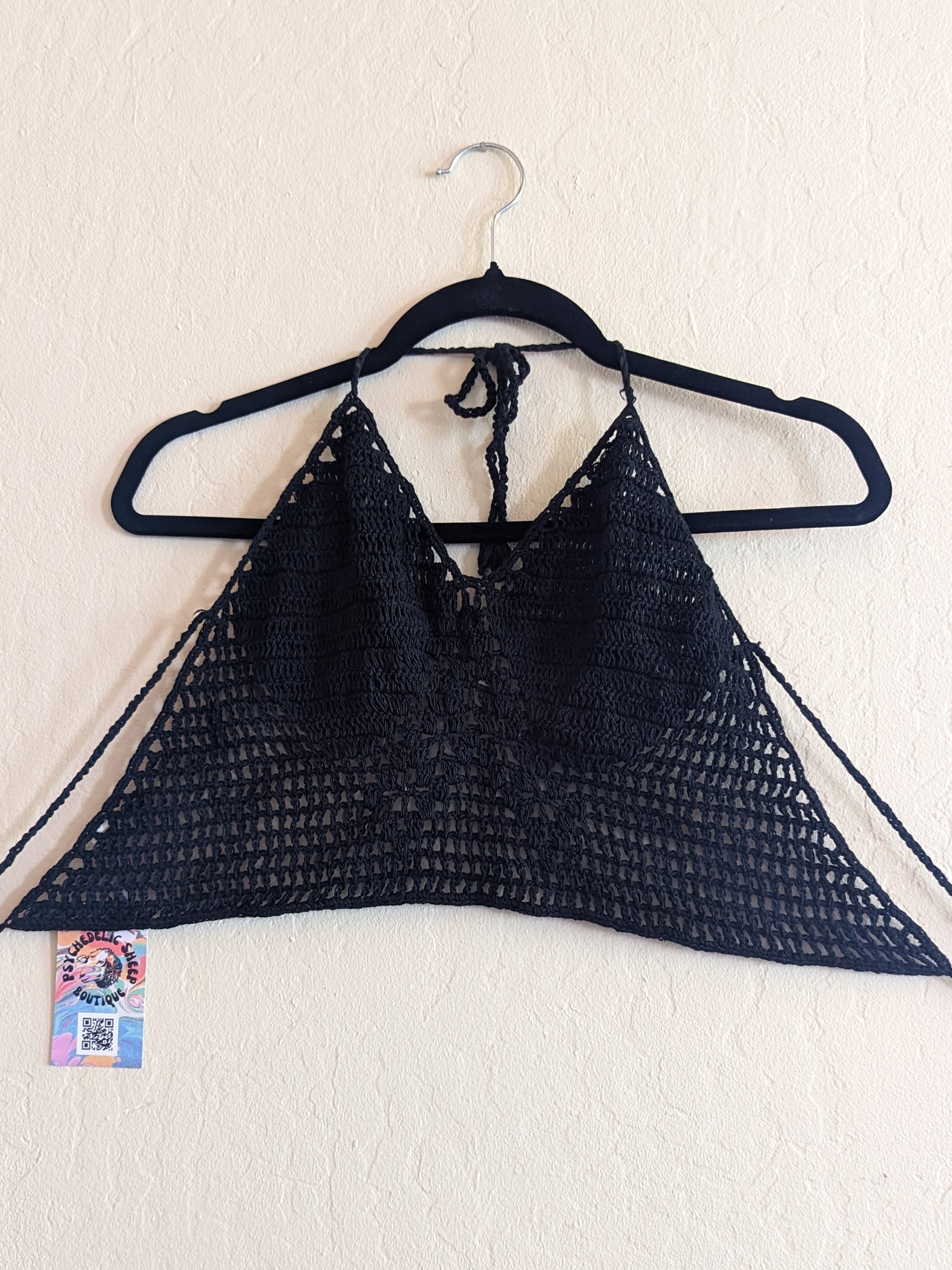 Black crochet top hung on a white wall.