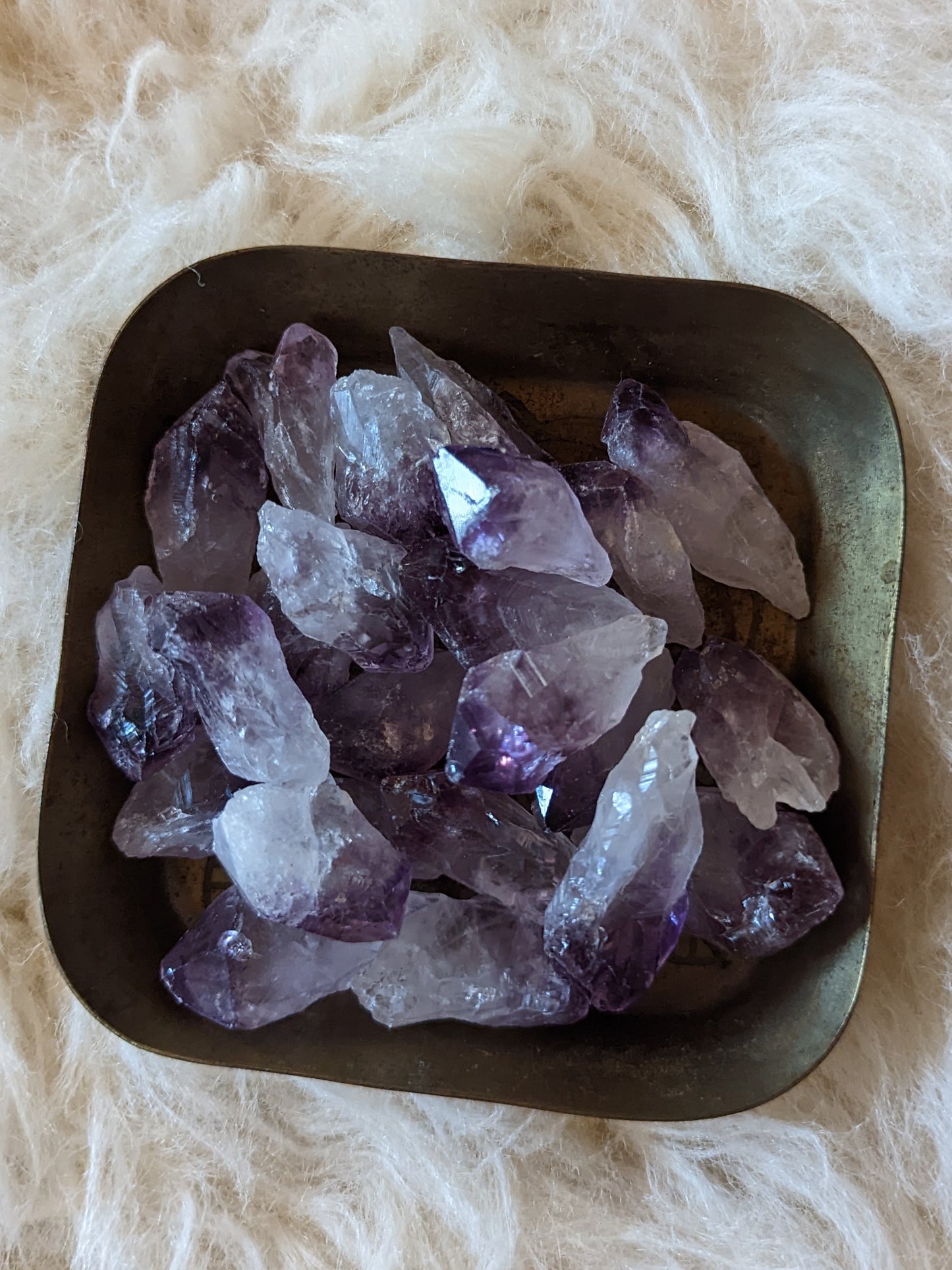 Amethyst crystals glisten in a sleek metal bowl, radiating enchanting shades of purple, captivating the eye.