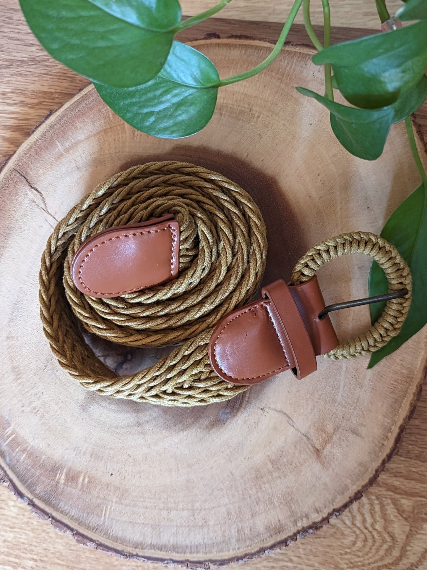 Yellow braided belt with brown leather details coiled up.