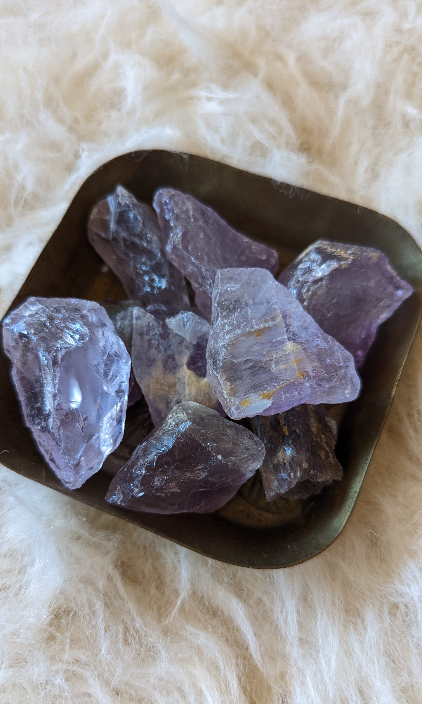 Amethyst crystals glisten in a polished metal bowl, showcasing their vibrant purple hues and natural beauty.
